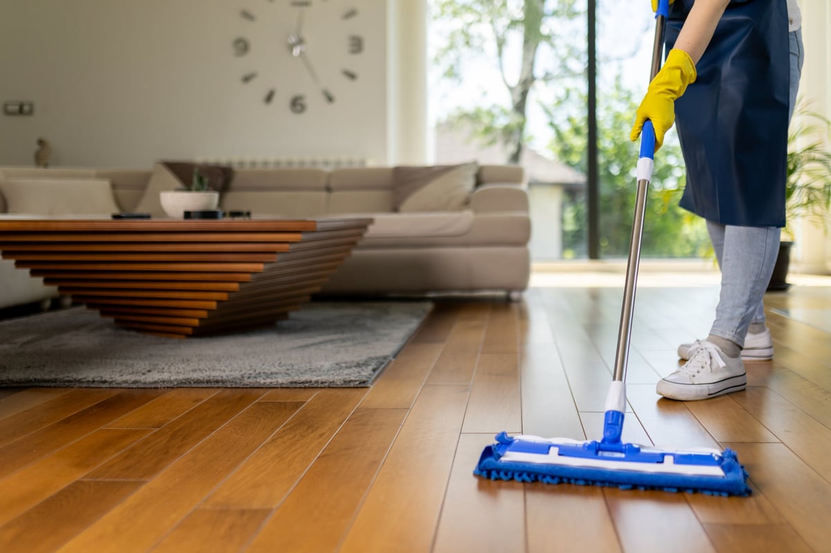 Professional cleaner mopping hardwood floors in bright modern living room with sunlight through windows