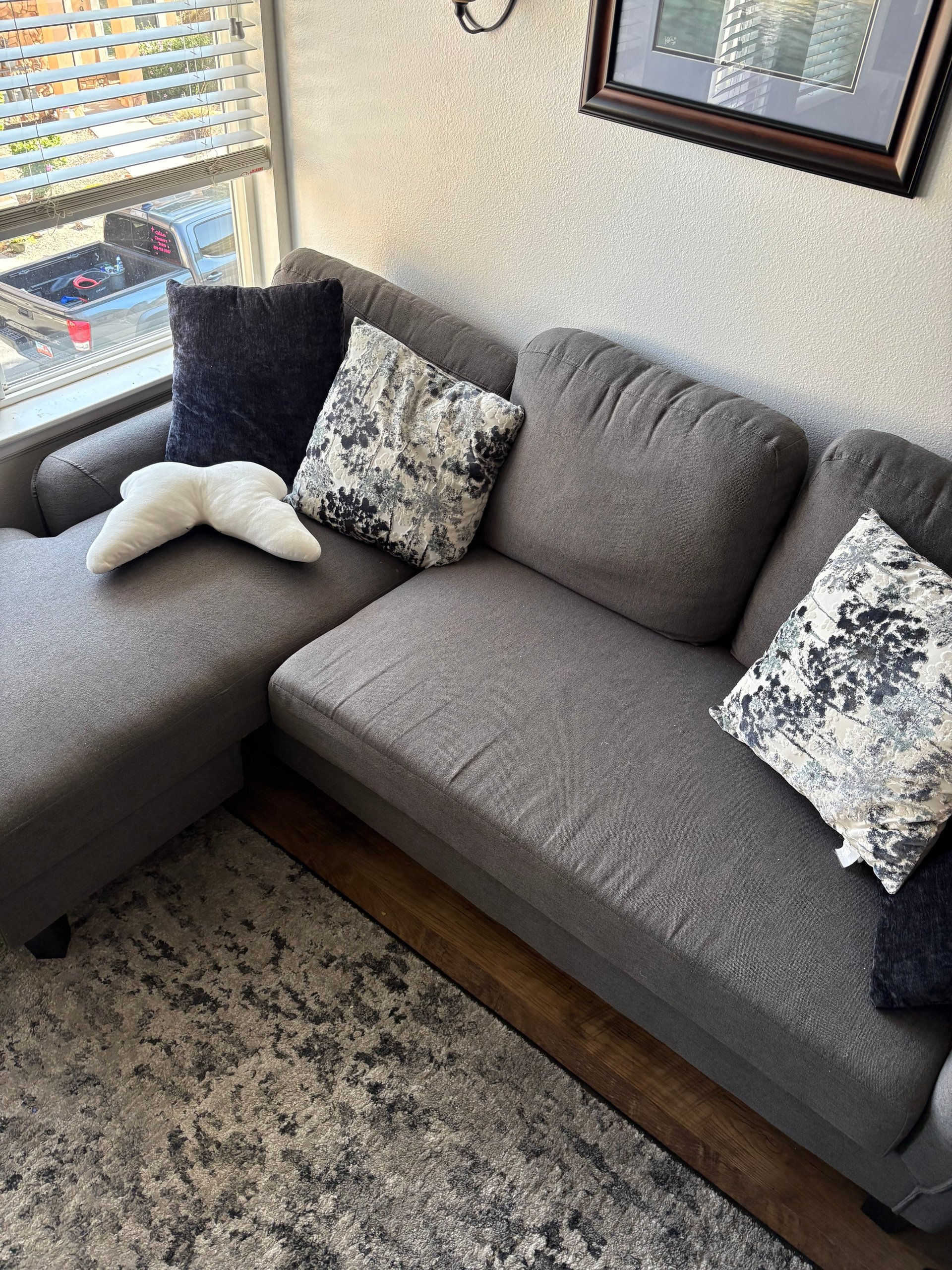 Gray sectional sofa with black and patterned throw pillows in a living room near windows and framed artwork