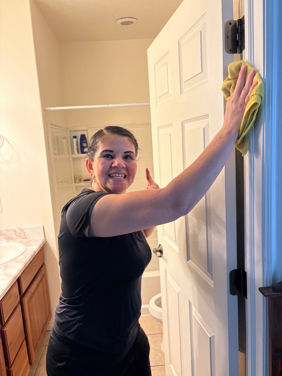 Woman cleaning a wall or door frame with a yellow cloth in a home hallway
