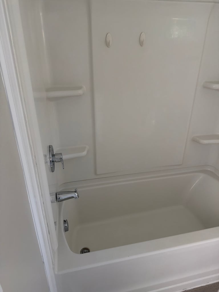 Empty white bathtub with shower enclosure and chrome fixtures viewed from above