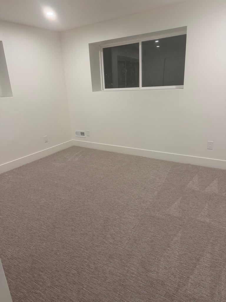 Empty room with beige walls, gray carpet flooring, and a large window with dark glass panels