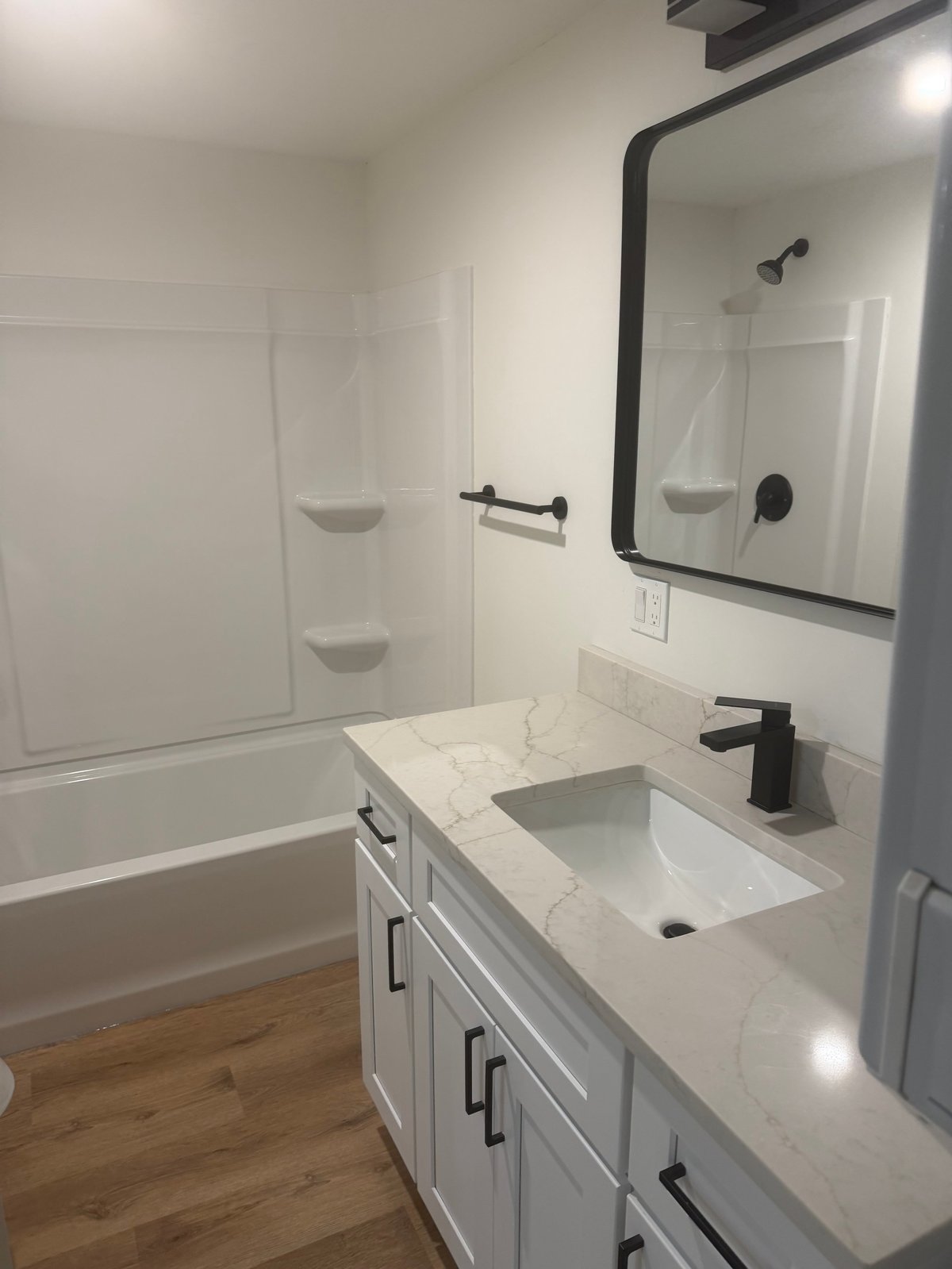 Modern bathroom with white vanity, sink with black faucet, framed mirror, and shower-tub combo with glass enclosure