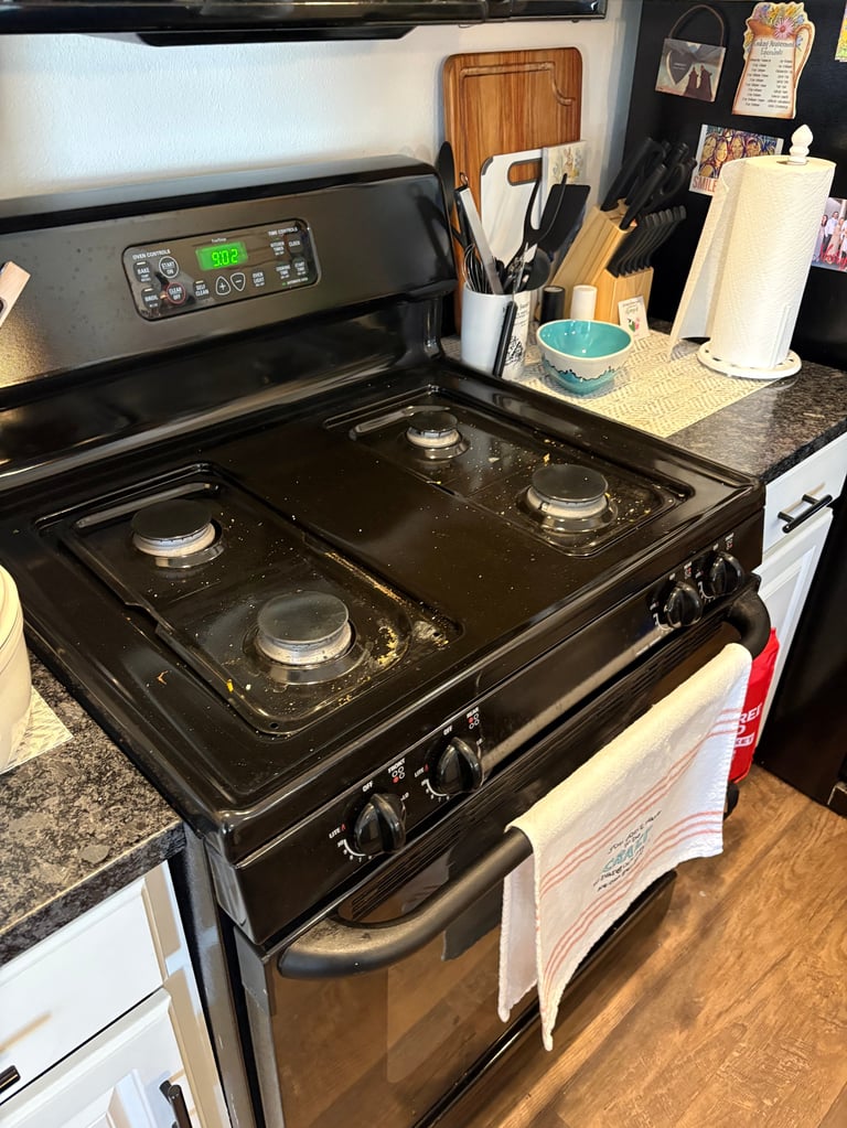 Black gas stove with four burners in a kitchen, with countertop storage and cooking utensils visible in the background