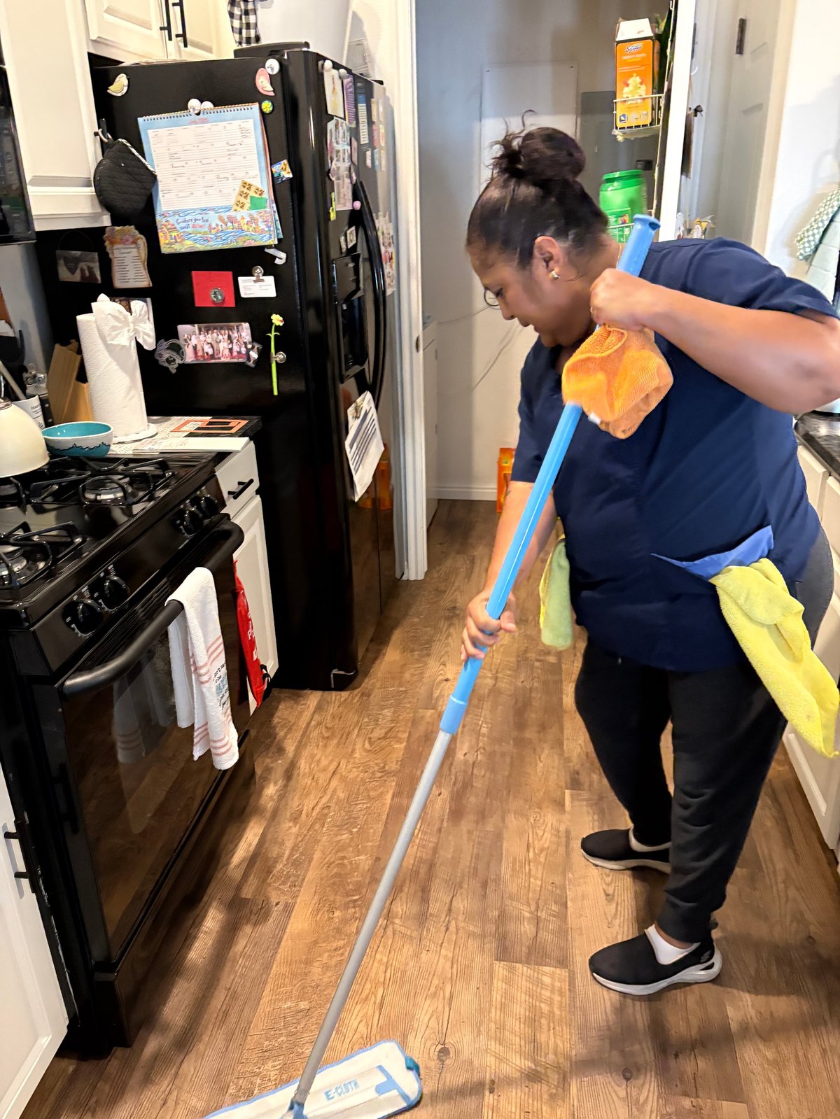Woman in navy shirt cleaning kitchen floor with mop and bucket