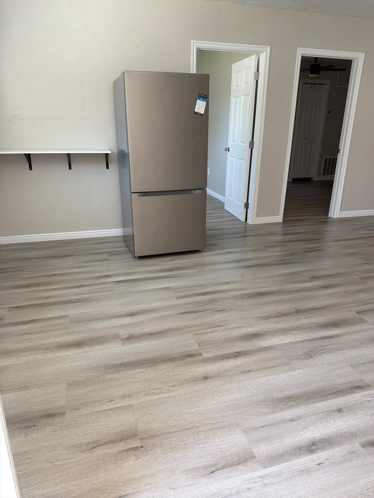 Stainless steel refrigerator in empty apartment with wood-look flooring, white walls, and two doorways