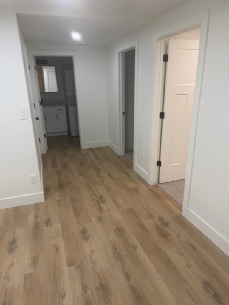 Empty hallway with hardwood flooring, white walls, and doors leading to adjacent rooms