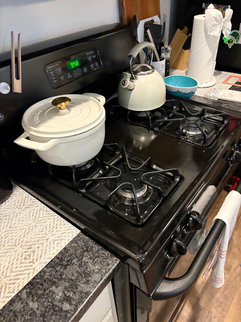 Black stovetop with white pot and cream kettle, kitchen counter with microwave and cooking utensils