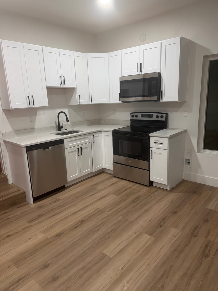 Modern white kitchen with stainless steel appliances, microwave, and wooden floor