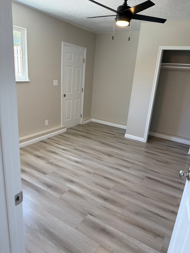 Empty bedroom with wood-look laminate flooring, beige walls, ceiling fan, and two closets with white trim